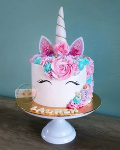 a white cake with pink and blue flowers on top, topped with a unicorn's face