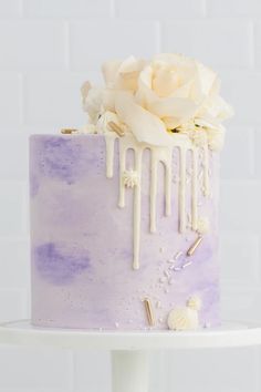 a purple and white cake with flowers on the top is sitting on a table in front of a white brick wall