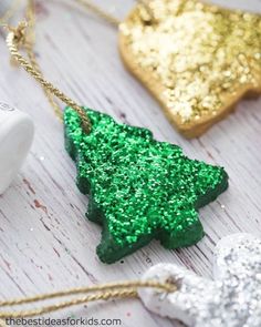 green glitter christmas tree ornament next to gold and silver ornaments on white wood