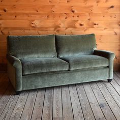 a green couch sitting on top of a wooden floor next to a wood paneled wall