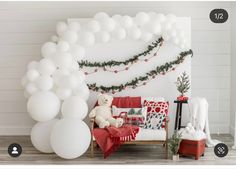 a room decorated for christmas with white balloons and garland on the wall, teddy bear sitting on a couch