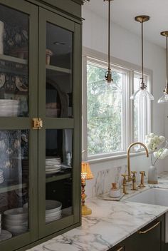 a kitchen with green cabinets and marble counter tops, gold faucets hanging from the ceiling