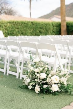 an outdoor ceremony setup with white chairs and flowers on the ground in front of them