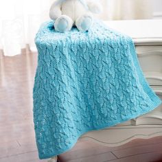 a white teddy bear sitting on top of a bed next to a blue knitted blanket