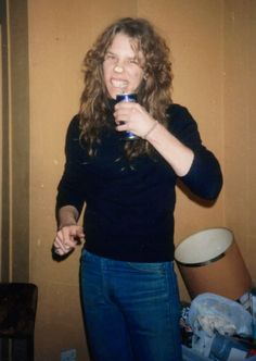 a woman holding a glass in her right hand and smiling at the camera while standing next to a wall