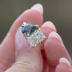 a person is holding an engagement ring with a blue and white diamond in it's hand