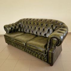 a green leather couch sitting on top of a tile floor next to a white wall