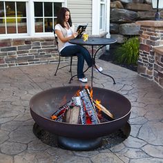 a woman sitting in front of a fire pit with a laptop on top of it