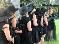 a group of women dressed in black standing next to each other wearing hats and dresses