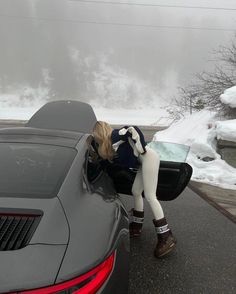 a woman leaning on the hood of a sports car with her feet in the window