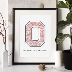 a framed poster with the letter o on it next to a potted plant and two white vases