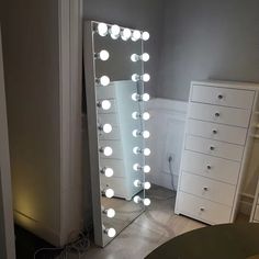 a large lighted mirror sitting on top of a wooden floor next to a white dresser