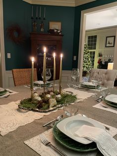 a dining room table set with place settings and candles