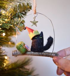 a hand holding a christmas ornament with a black cat wearing a party hat