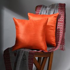 two orange pillows sitting on top of a wooden chair