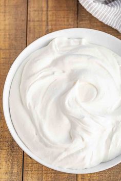 a white bowl filled with whipped cream sitting on top of a wooden table next to a towel