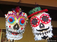 two paper skulls with hats and flowers on their heads are hanging from the ceiling in front of a building