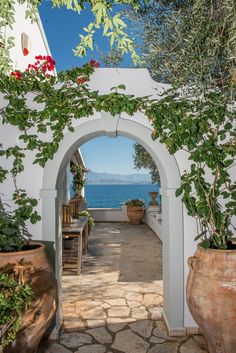 an archway leading to the ocean with potted plants on either side and benches at the end