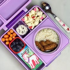 a purple lunch box filled with rice, fruit and veggies next to a spoon