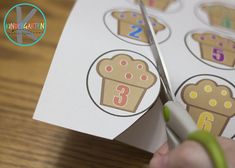 a person cutting through some stickers with scissors on a wooden table next to a piece of paper