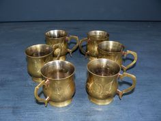 six antique brass coffee mugs on a blue table