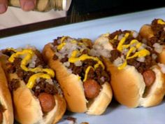 four chili dogs with mustard and onions on them are lined up in a row, ready to be eaten