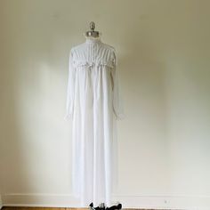 This beautiful long white nightgown evokes the Victorian era with its feminine and delicate details. Made from soft, breathable 100% cotton, it features long sleeves with ruffled cuffs and a high collar trimmed in eyelet lace. It gathers at the yoke which is also trimmed in white eyelet lace, creating a timeless vintage silhouette. The back fastens with three white buttons for an old-world charm.  Expertly sewn, Victorian nightgown. Treat yourself to a historic experience or delight someone who loves 19th century fashion with this charming gown. X Small size Measurements with an inch of room for comfort Please note that the armholes and shoulders are narrow Bust up to 21" Waist and hips free Exact measurements are taken flat to compare to a garment that fits well. Length: 50" Shoulders acr Long Sleeve White Nightgown For Sleep, White Long Sleeve Nightgown For Sleep, White Long Sleeve Nightgown For Daywear, White Long-length Sleepwear For Loungewear, White Lace Trim Nightgown For Home, White Fitted Nightgown For Bedtime, White Lace Trim Gown For Daywear, Fitted White Nightgown For Bedtime, Fitted White Sleep Gown