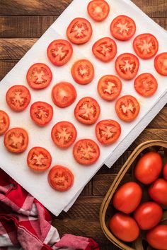 fresh tomatoes on a cutting board next to a basket of green beans and a cloth