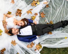 a bride and groom laying on the ground in their wedding gowns with leaves all over them