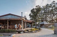 people are sitting at the table outside of a small cabin style house with gravel driveway