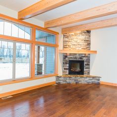 an empty living room with wood flooring and stone fireplace in the center surrounded by large windows