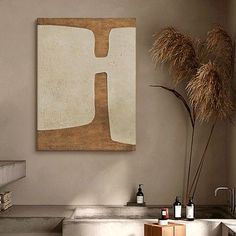 an abstract painting hangs on the wall next to a vase with dry grass in it