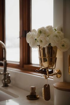 white flowers are in a gold vase on the sink