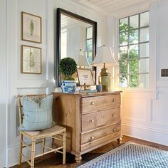 a room with a dresser, mirror and lamp on it's side table in front of a window