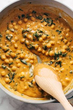 a wooden spoon in a pot filled with chickpeas and spinach