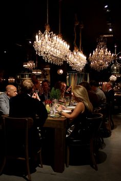 a group of people sitting at a table in a room with chandeliers hanging from the ceiling