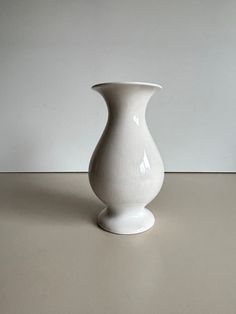 a white vase sitting on top of a table next to a gray wall and floor