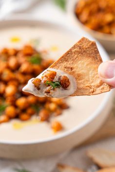 a hand holding a cracker over a bowl of chickpeas