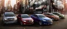 four different colored cars are parked in front of a large screen on the side of a building