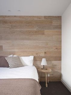 a bed sitting in a bedroom next to a lamp and wooden headboard on a wall