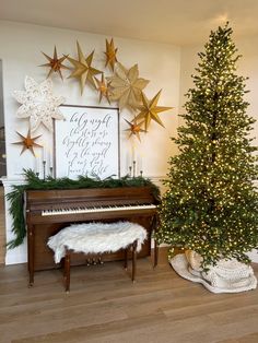 a christmas tree sitting next to a piano in front of a wall with gold stars on it