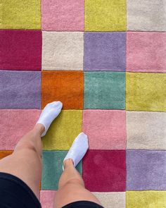 a woman's feet in white shoes on a multicolored rug with squares