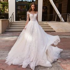 a woman in a white wedding dress standing on the sidewalk with her arms behind her back