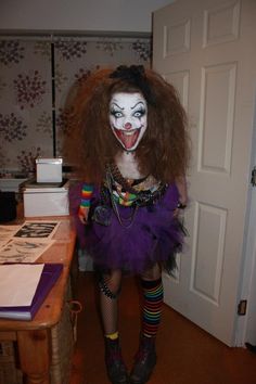 a woman dressed as a clown standing next to a table