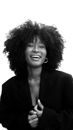 a black and white photo of a woman with curly hair smiling at the camera while holding her hands together