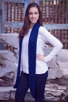 a woman standing in front of a wooden fence wearing a blue knitted scarf and white sweater