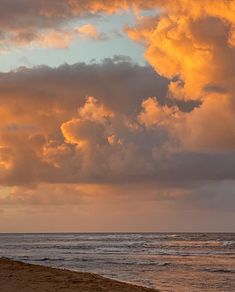 two people are walking on the beach with their surfboards under an orange and blue cloudy sky