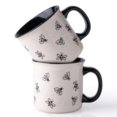 two black and white coffee mugs with bees on them are stacked in front of each other