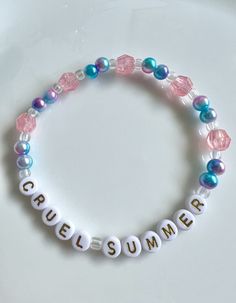 A handmade friendship bracelet with golden letters spelling out cruel summer, surrounded by pink and blue pearl beads, and pink and iridescent crystal beads. Taylor Swift Friendship Bracelet Blue, All To Well Bracelet, All Too Well Bracelet Taylor Swift, Beaded Bracelets Letters, All Too Well Friendship Bracelet, The Eras Tour Friendship Bracelets, All Too Well Bracelet, Friendship Bracelets Pink, Diy Bracelets Beads