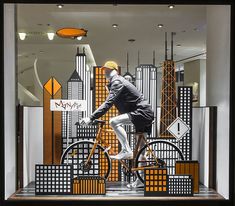 a mannequin riding a bike in front of a window display with cityscapes